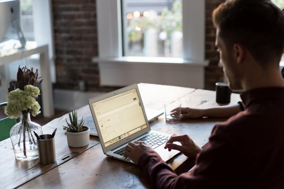Small-business owner working on a laptop at a wooden desk by a window