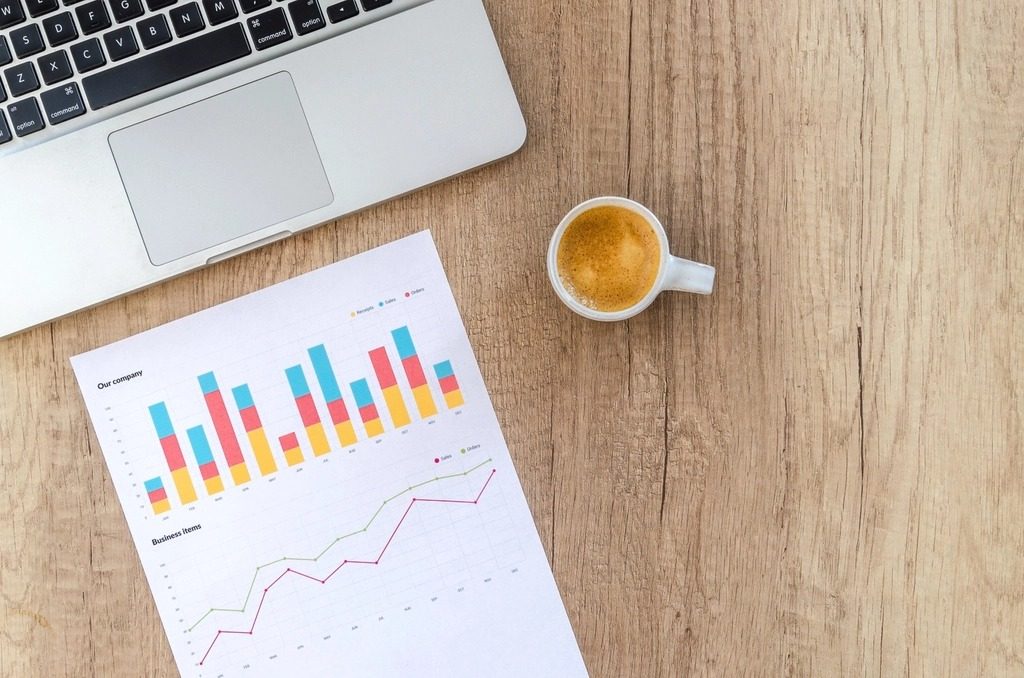 Printed sales charts and a coffee on a wooden desk next to a laptop